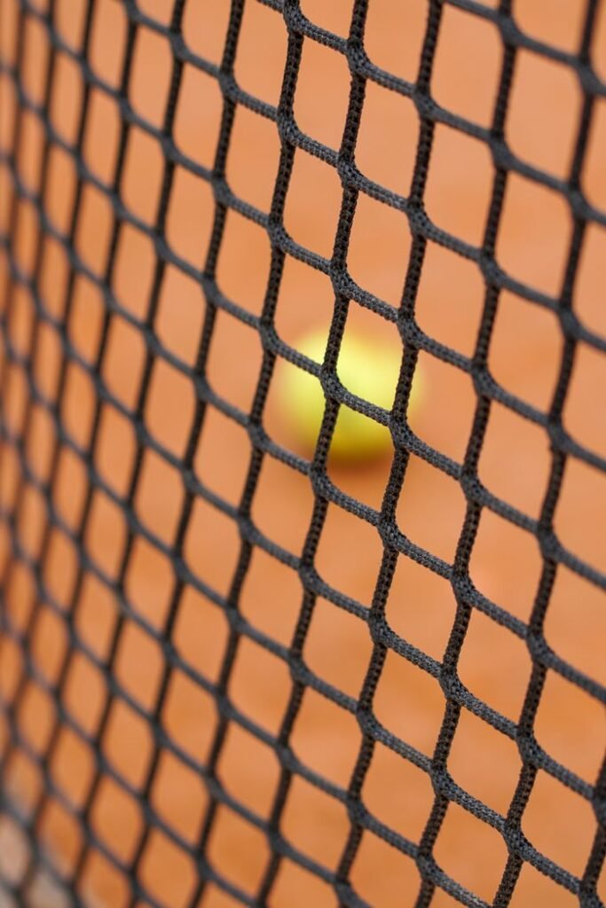 Tennis ball behind net on a clay court capturing sports essence.