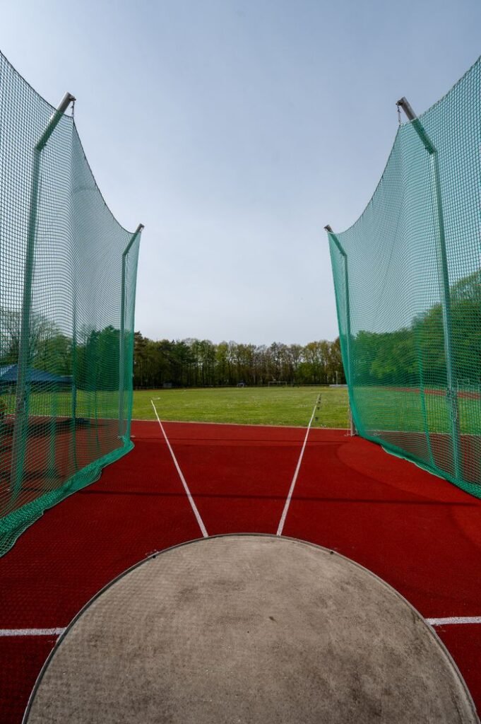 View of a throwing circle in an athletics stadium with nets and grassy field.