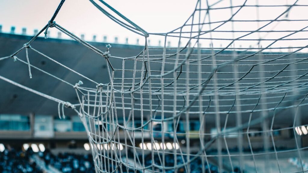 A detailed view of a soccer net with stadium seating in the background.