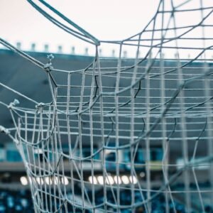 A detailed view of a soccer net with stadium seating in the background.
