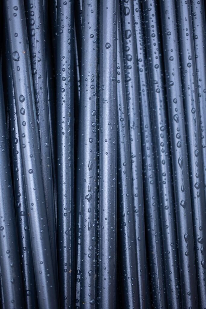An abstract close-up of vertically arranged wet black pipes with raindrops.